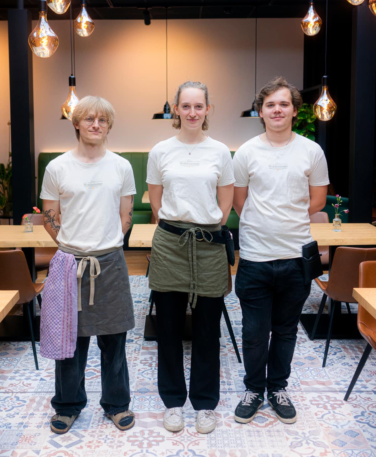 Das Team von Dein Wohnzimmer in cremefarbenen Logo-Shirts im Gastraum mit Pendelleuchten